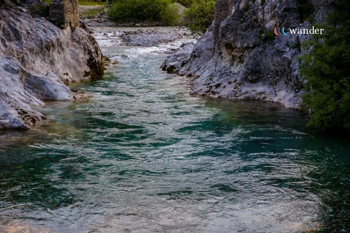 A clear mountain stream flowing between rocky cliffs with greenery on both sides.
