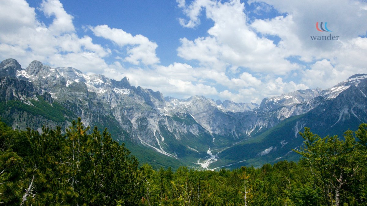 Scenic mountain landscape with snow-capped peaks, green valleys, and a blue sky with clouds.