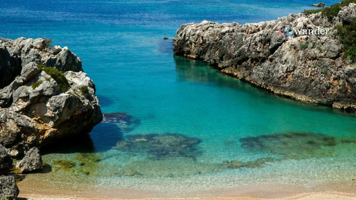 A serene cove with clear turquoise water surrounded by rocky cliffs and a sandy beach.