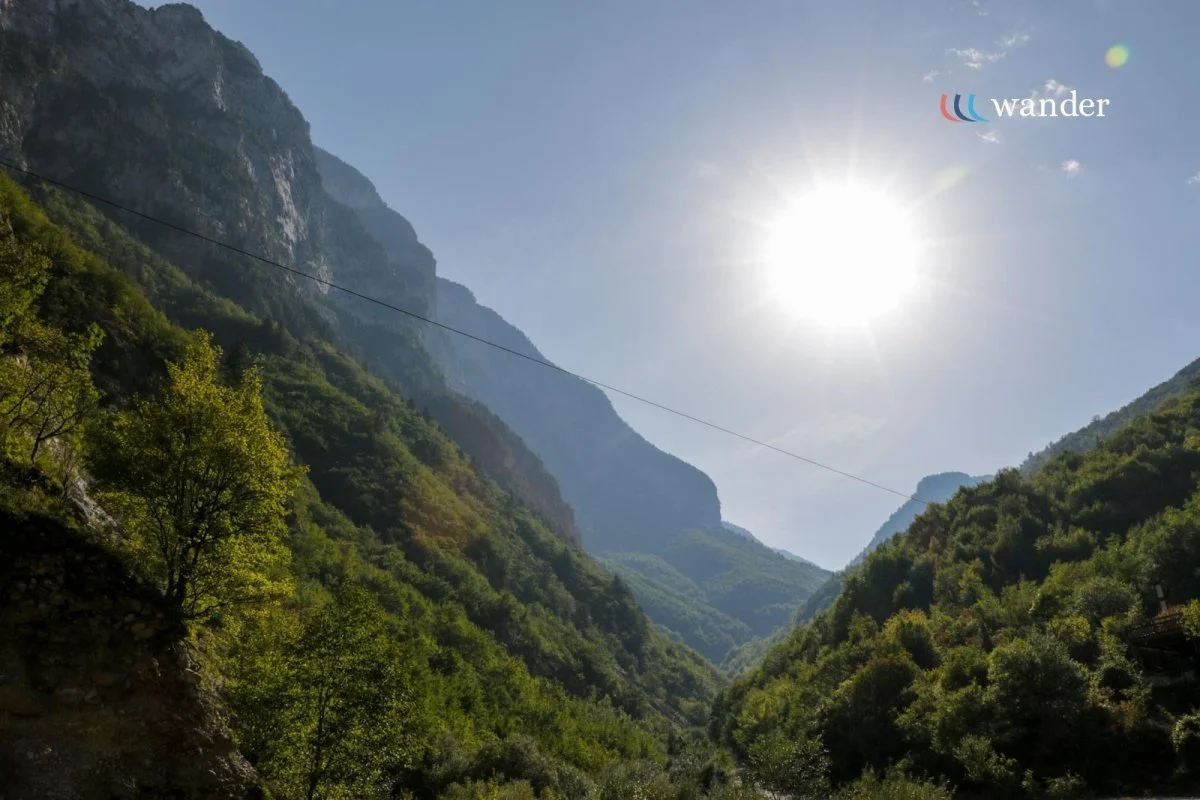 Sun shining over lush green mountains and a deep valley with trees.