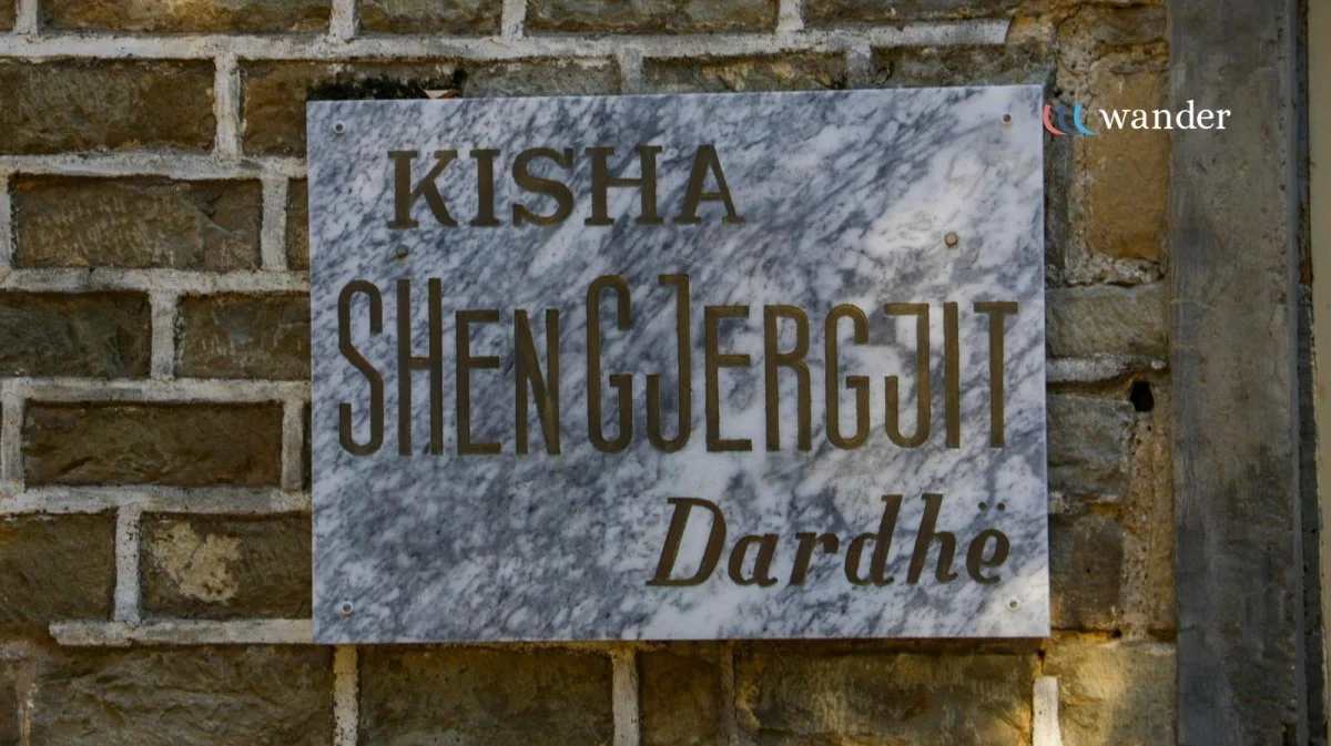 Marble plaque with the inscription 'KISH SHENG GU ER GUT Dardhe' mounted on a brick wall.