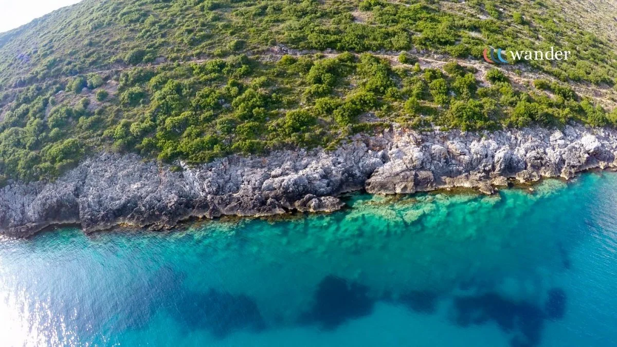 Aerial view of a rocky coastline with green vegetation and clear turquoise water.
