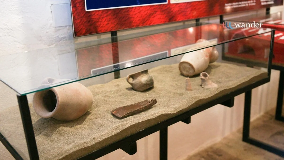 Ancient pottery and artifacts displayed in a museum glass case with sandy base.
