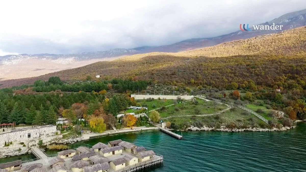 A landscape of a mountain with trees in fall colors, a green hillside, and a waterfront with houses and a dock.