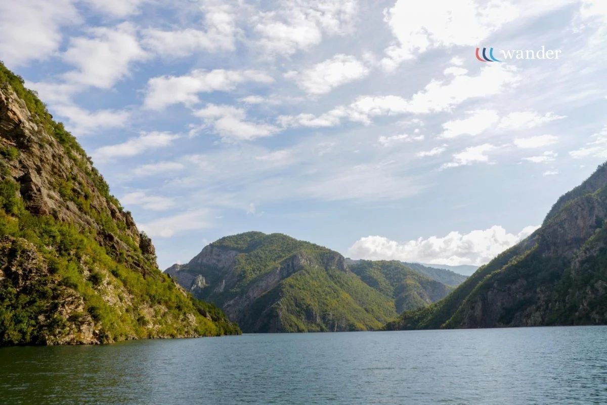 A scenic view of a river flowing between green, forested mountains under a partly cloudy sky.