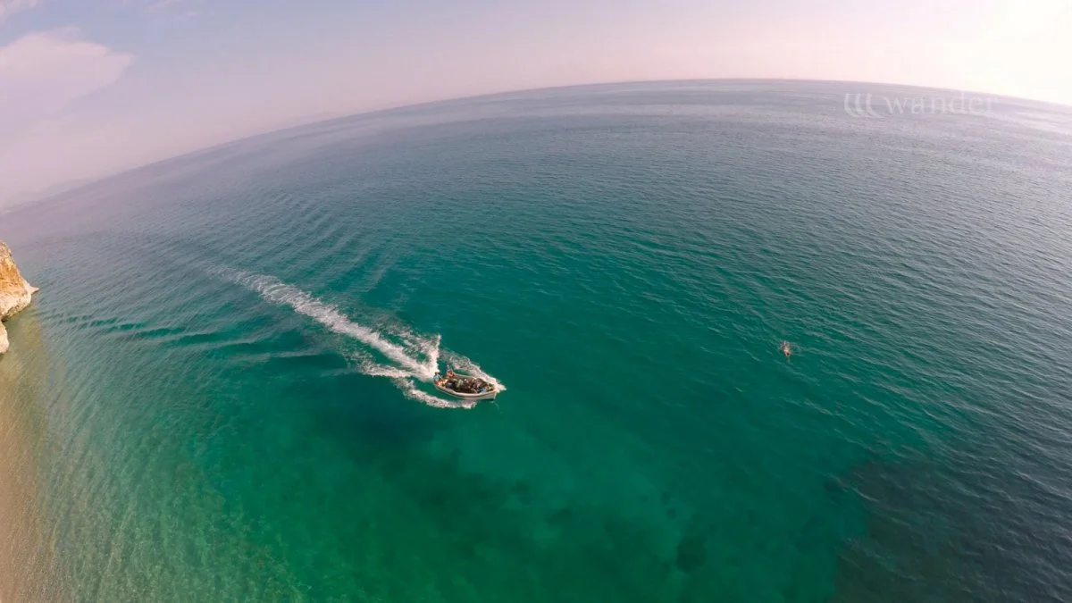 A boat sailing in the ocean near a rocky coastline with clear blue water.