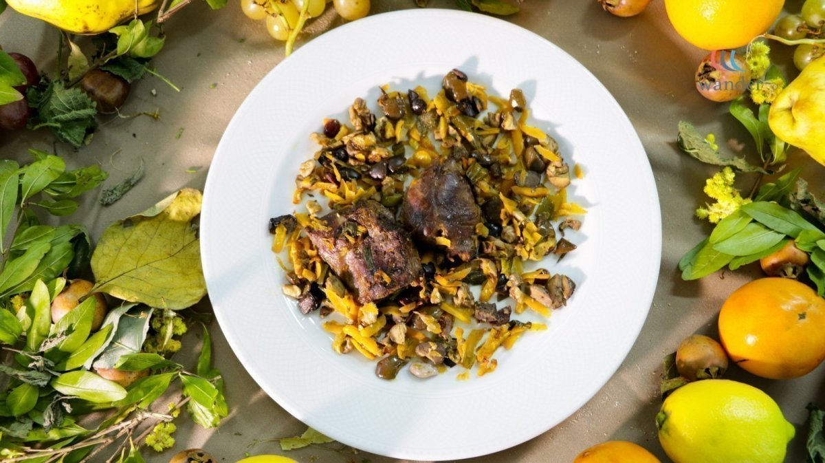 A white plate with cooked meat and chopped vegetables surrounded by colorful fruits and leaves.