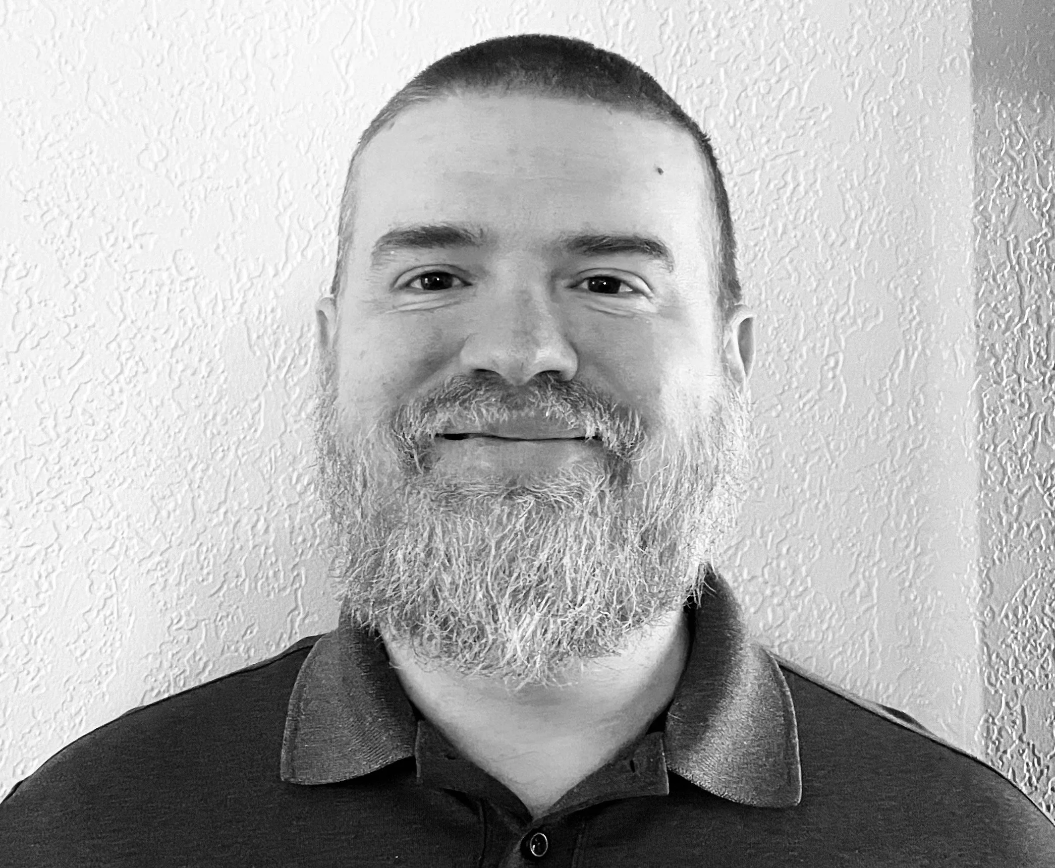 Black and white portrait of a smiling man with a beard wearing a collared shirt.