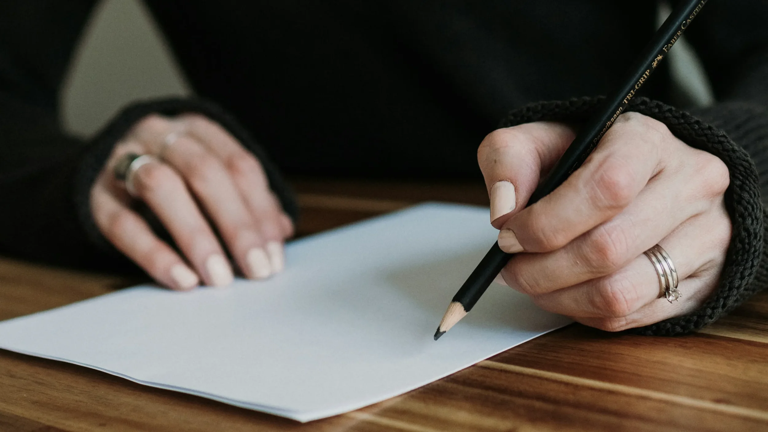 Woman sitting at table with pencil and paper ready to write something down