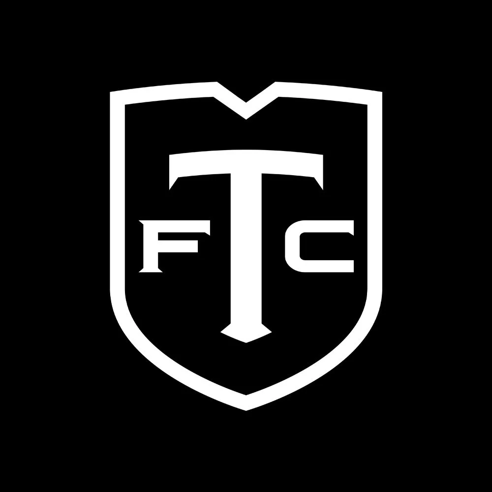 Black and white logo featuring a shield with a large letter T in the center and smaller letter F and C on either side.
