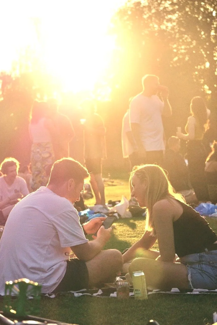 A family gathered outdoors during sunset, sitting on blankets and standing