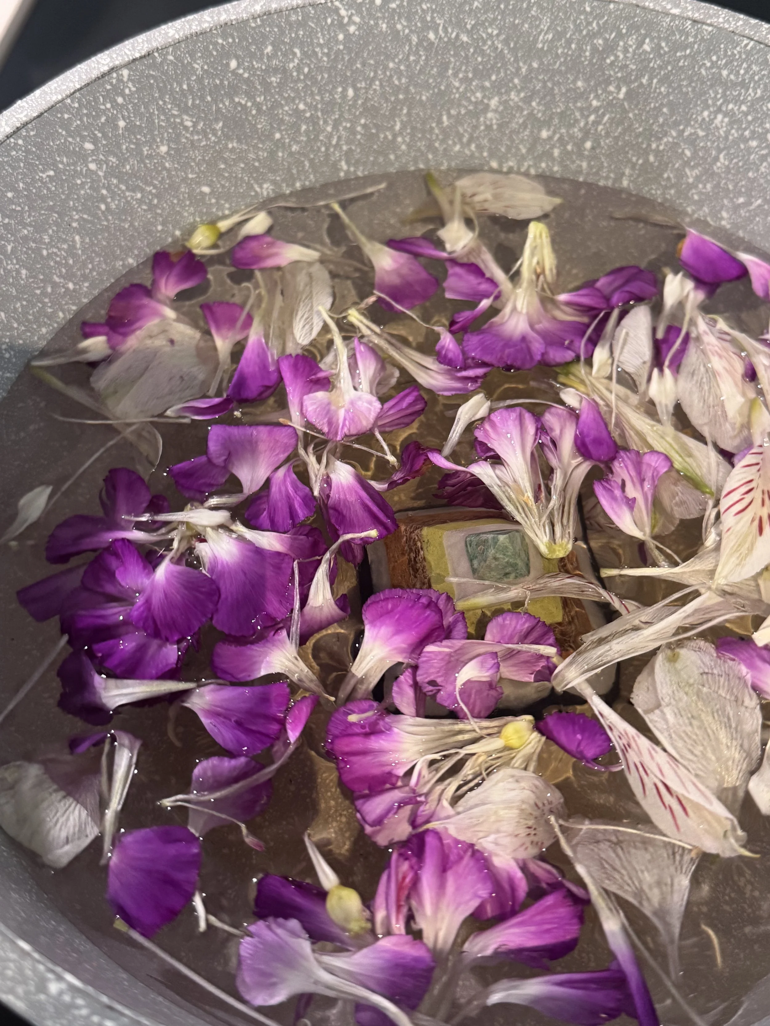 Purple and white flower petals soaking in water in a pot.