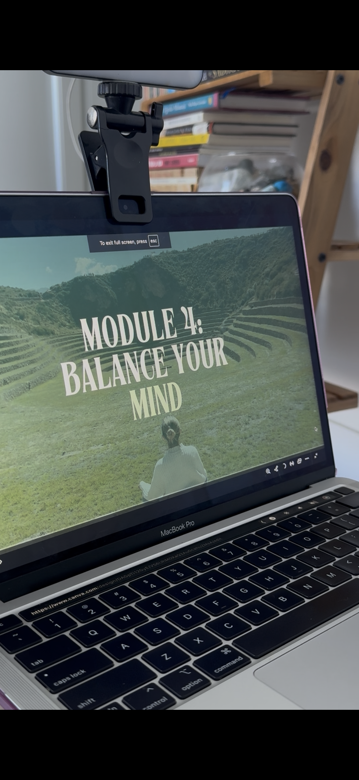 Laptop screen displaying a presentation slide titled 'Module 4: Balance Your Mind' with a background image of terraced fields and a person practicing yoga or meditation outdoors, with a bookcase in the background.