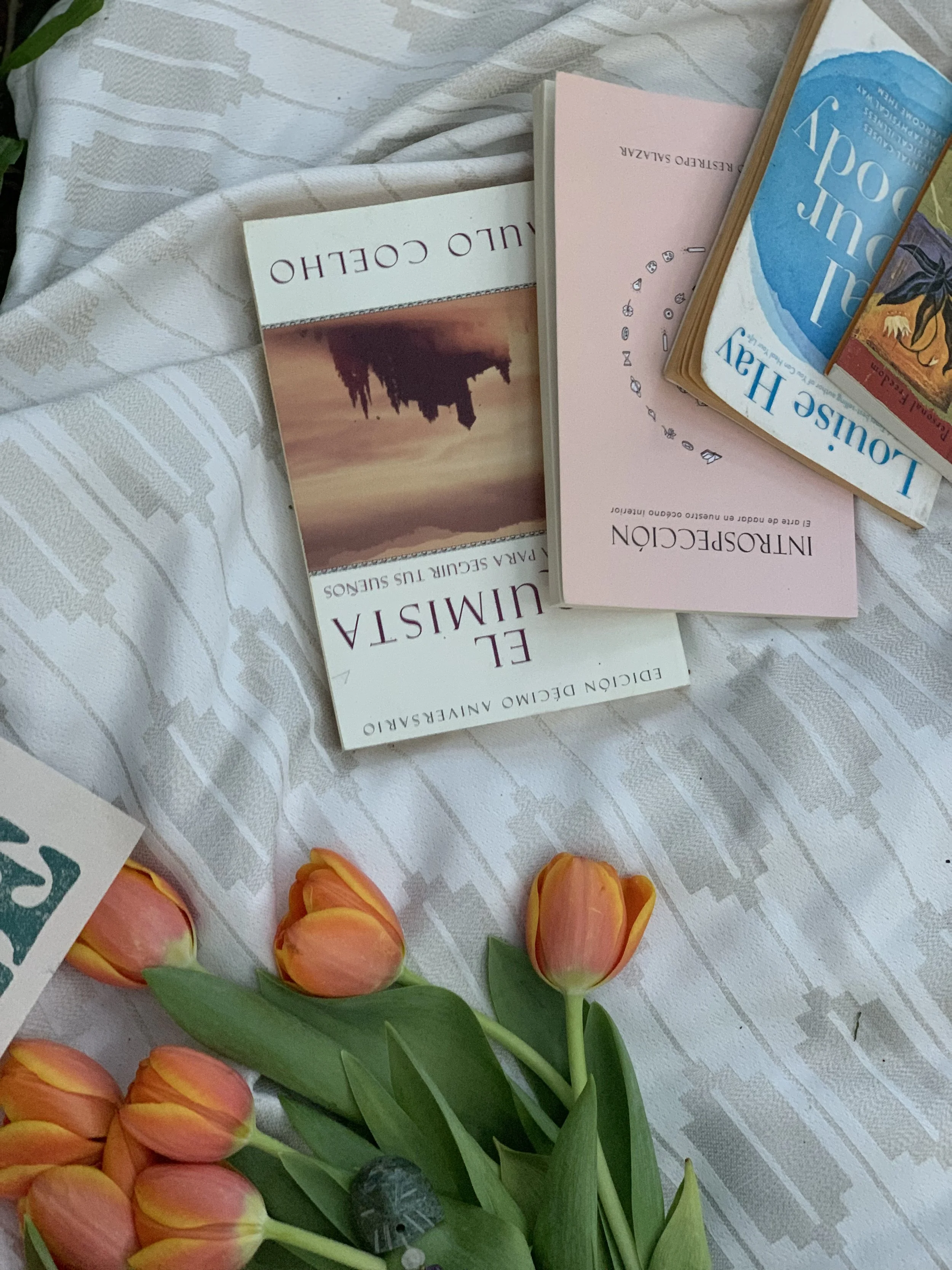 A close-up of a white patterned tablecloth with pink tulips and various books and pamphlets placed on it.