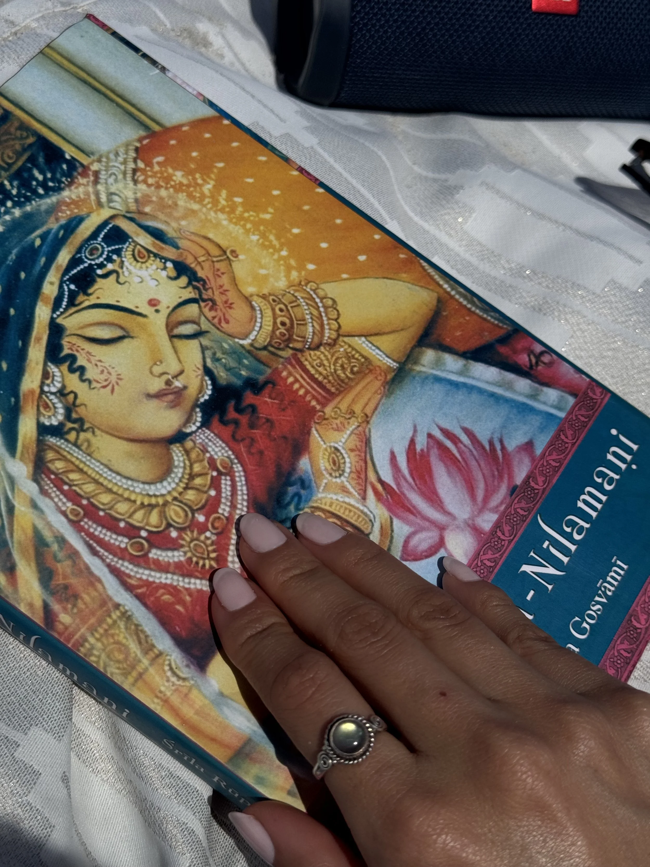 A person's hand with a ring on the middle finger resting on a book cover about Hindu goddess Durga, featuring an illustration of a female deity with jewelry, a red garment, and a lotus flower.