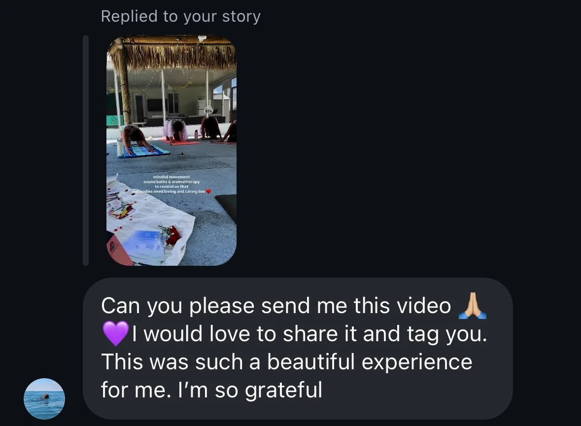 People practicing yoga on mats outdoors under a thatched roof, with a table of flowers and documents in the foreground.