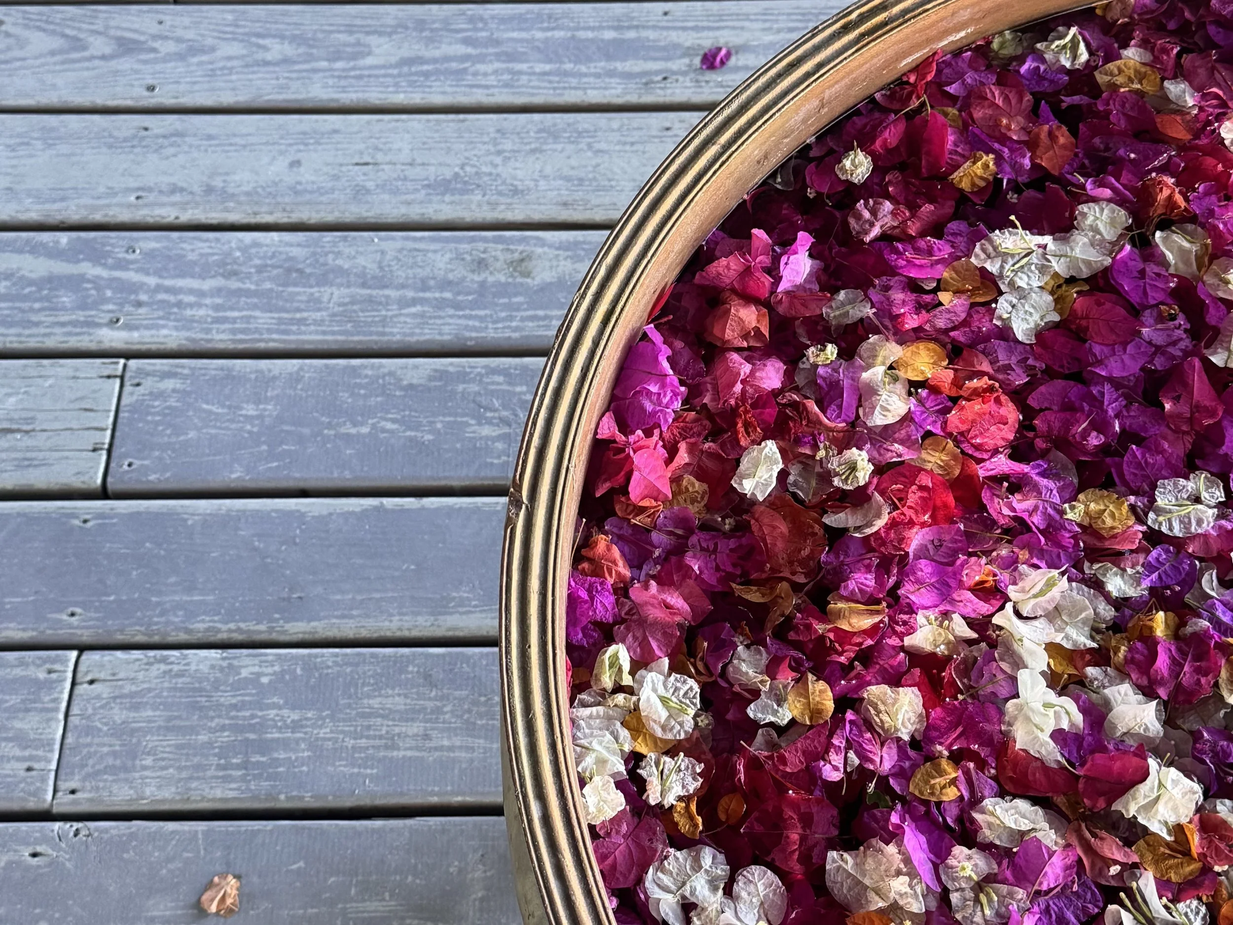 A wicker basket filled with colorful flower petals on a wooden surface.