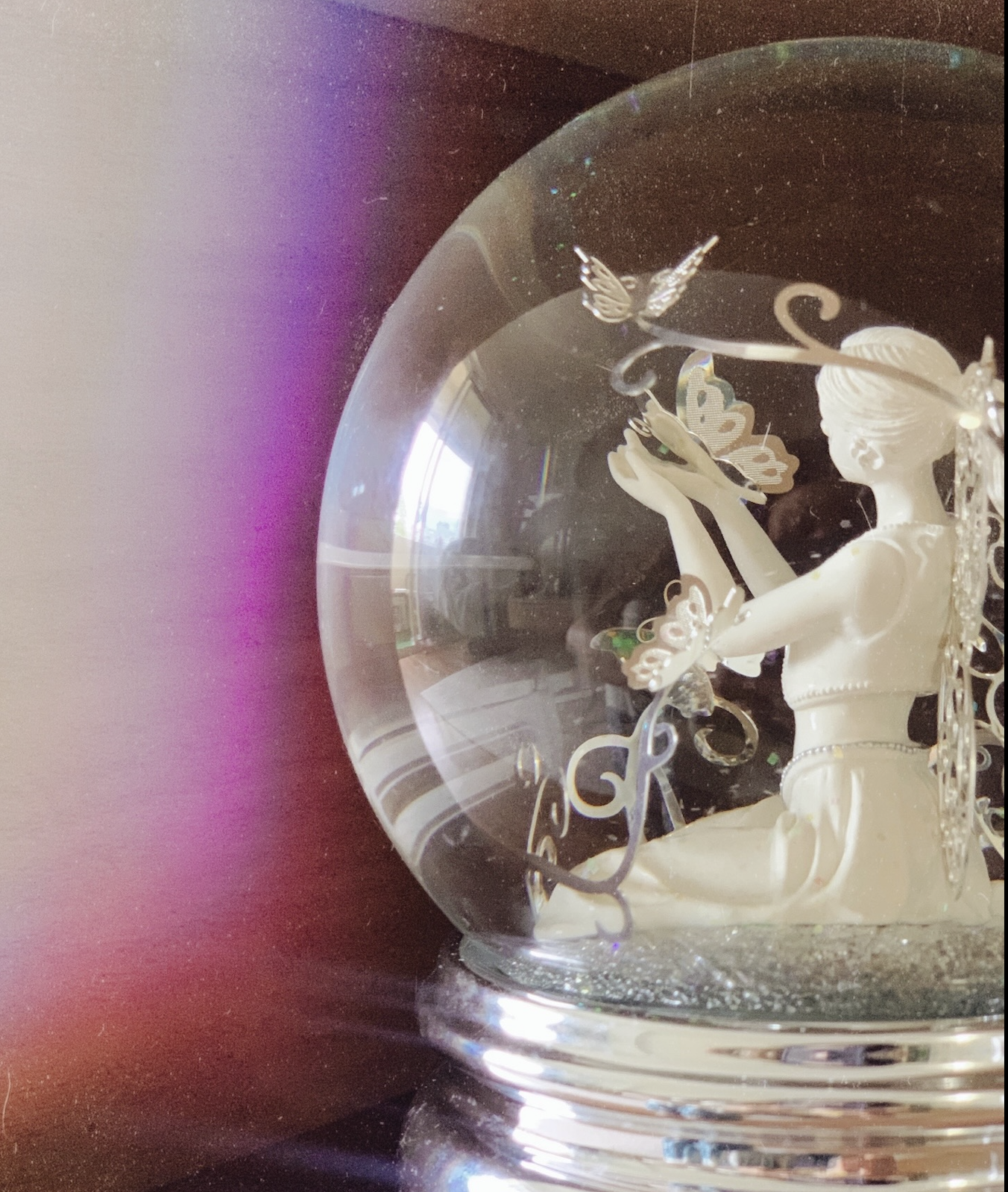 A decorative snow globe featuring a white figurine of a girl with butterflies around her.