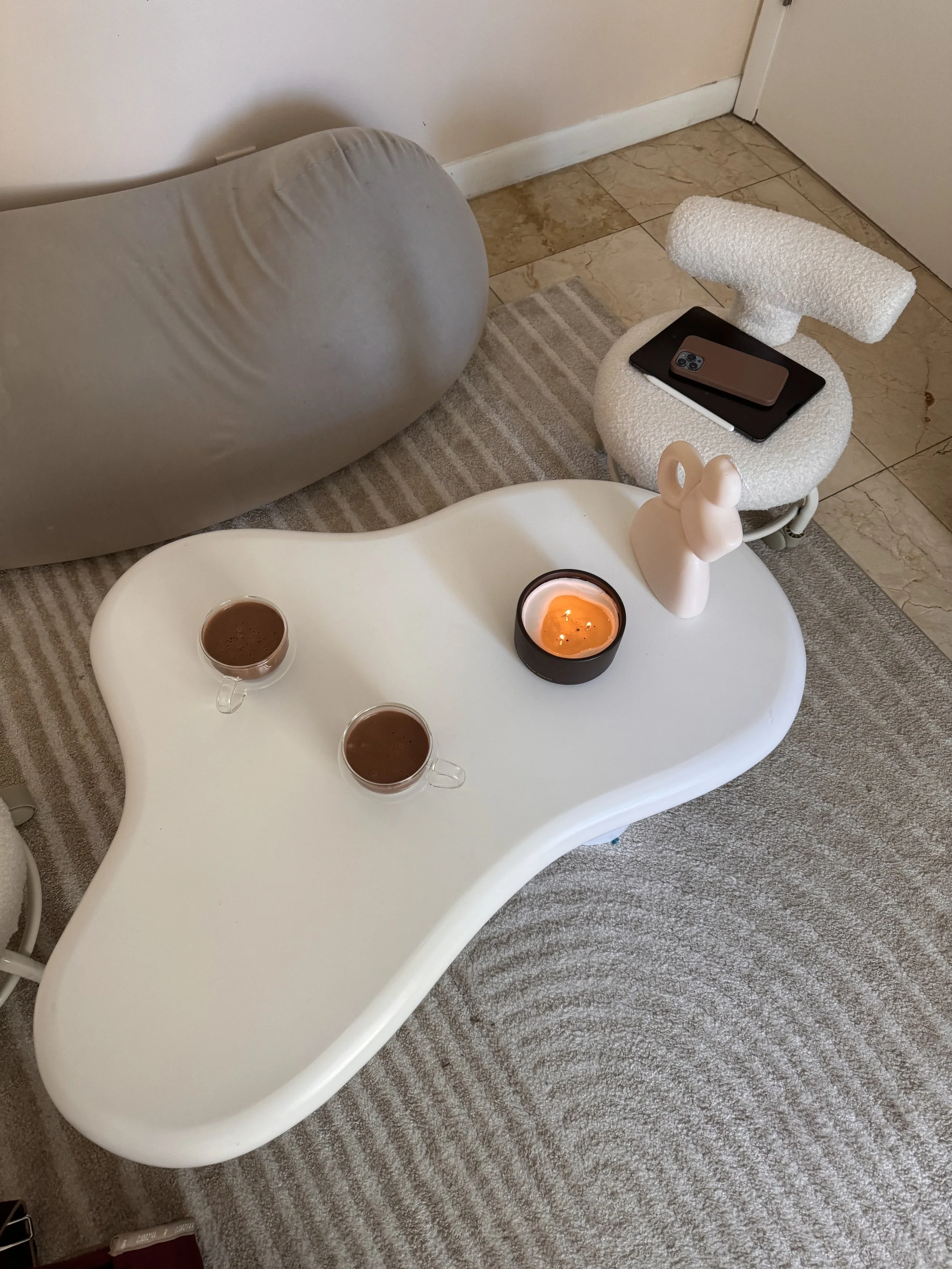 Coffee table with two cups of coffee, a candle, and a decorative headset figurine, with a sofa and a side chair in the background.