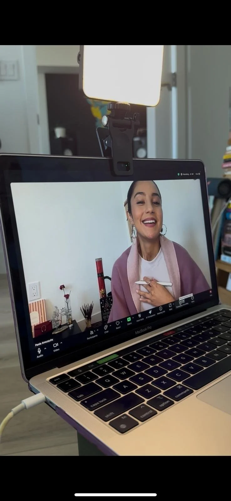 A woman smiling during a video call on a MacBook Pro laptop, with a ring light above her.