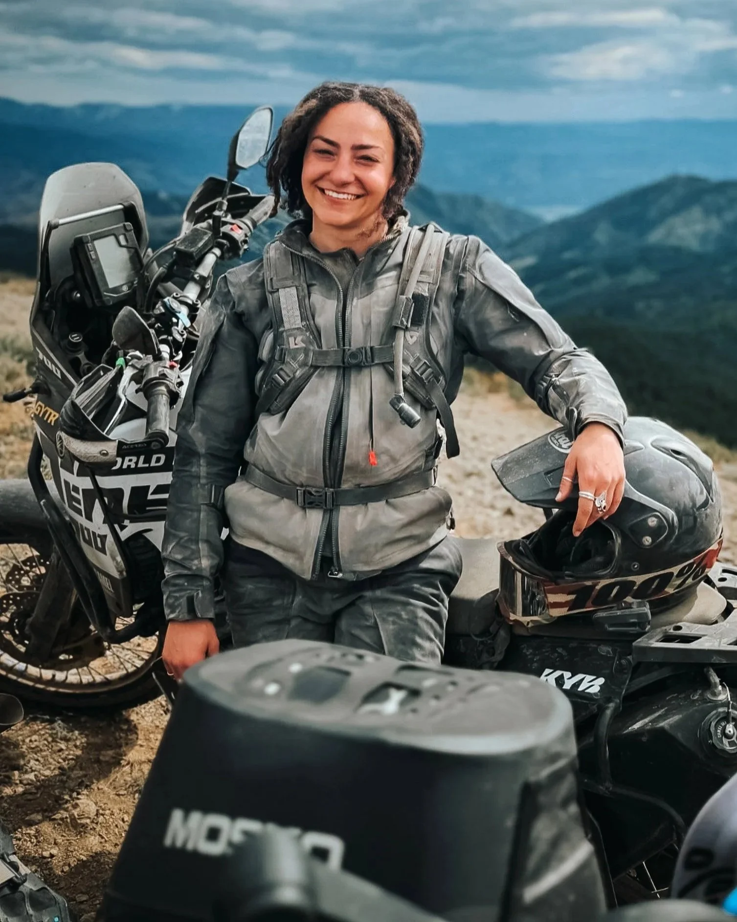 Woman in motorcycle gear standing beside her adventure bike on a mountain trail in Northern BC.