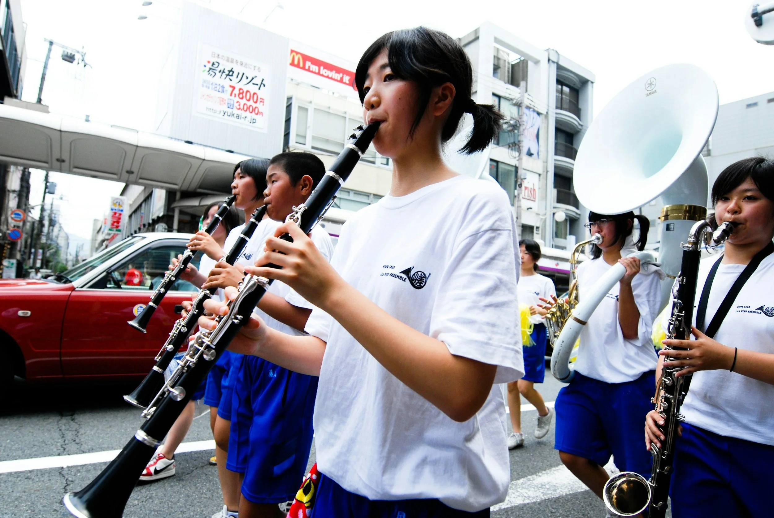Young students marching in a parade playing clarinets and saxophones on a city street.