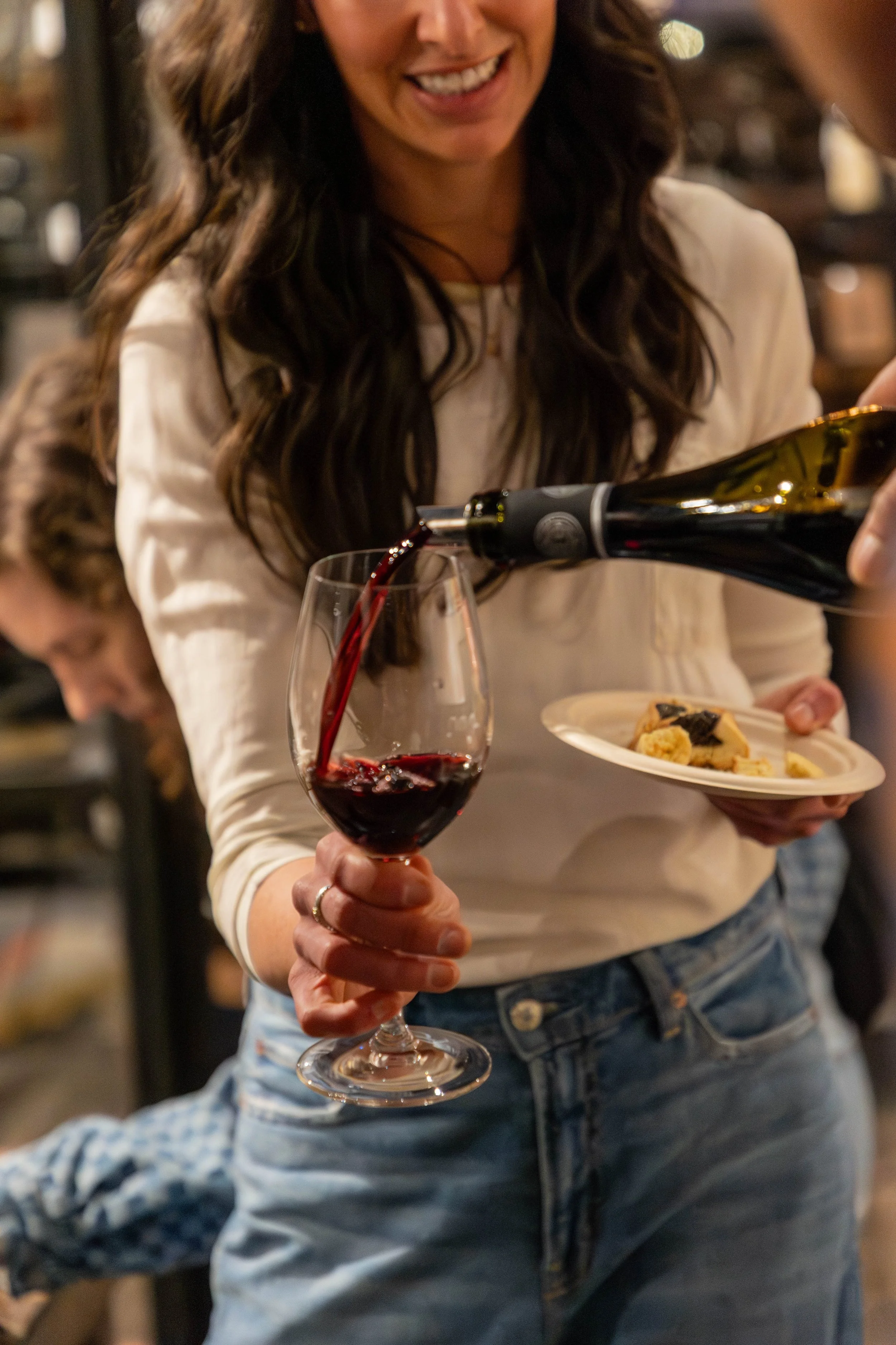 Woman pouring red wine into a glass at a social gathering.