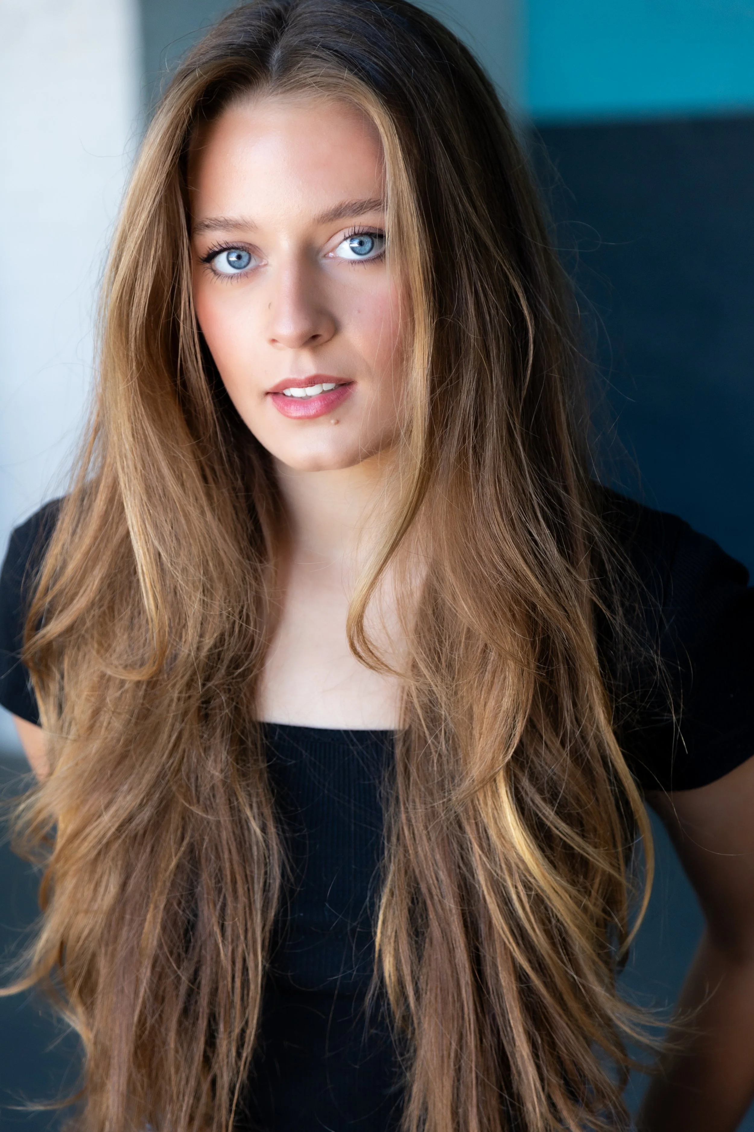 A young woman with long, wavy brown hair and blue eyes wearing a black top.