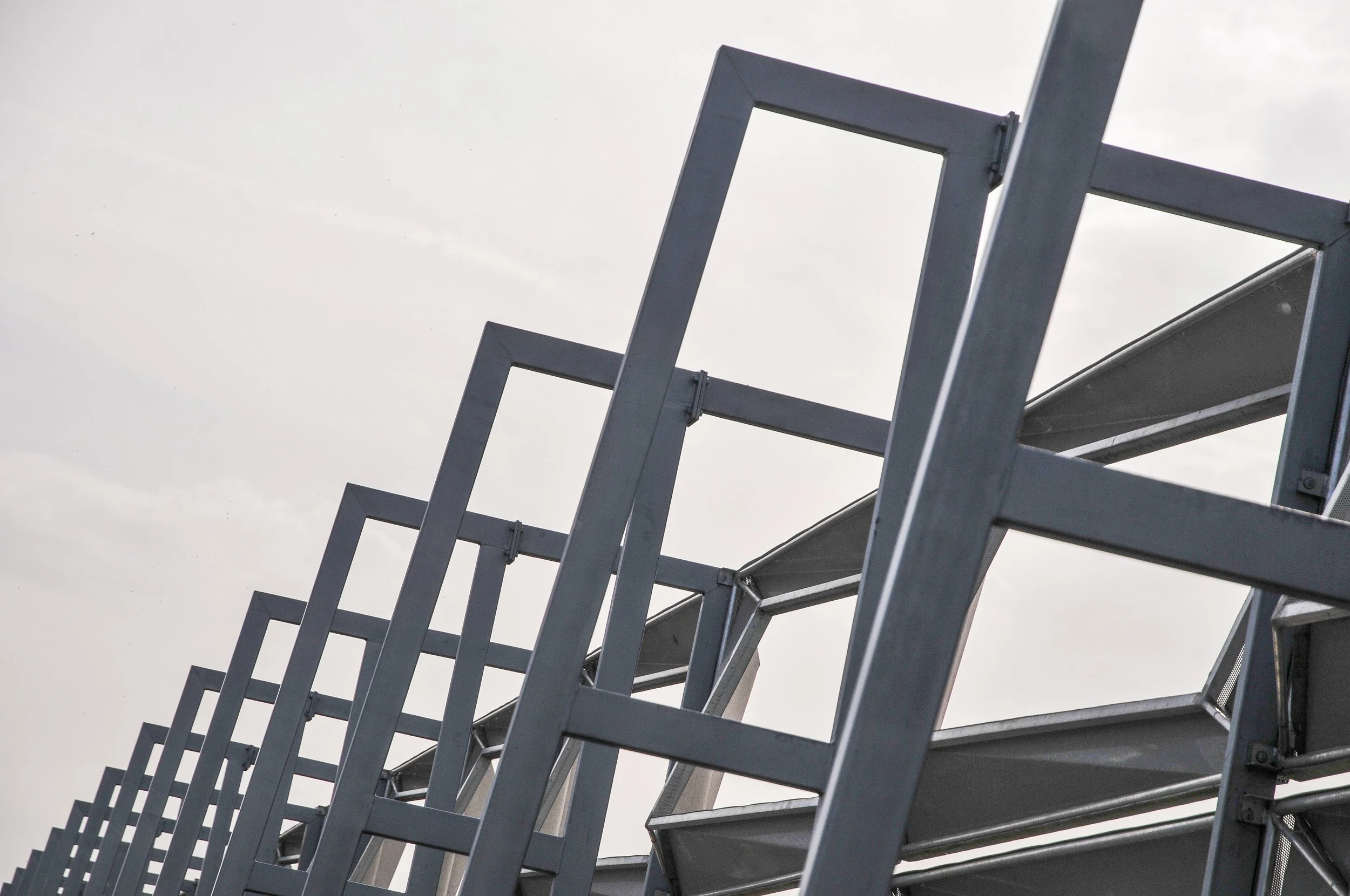 A close-up view of metal ladders or staircases with rectangular frames against an overcast sky.