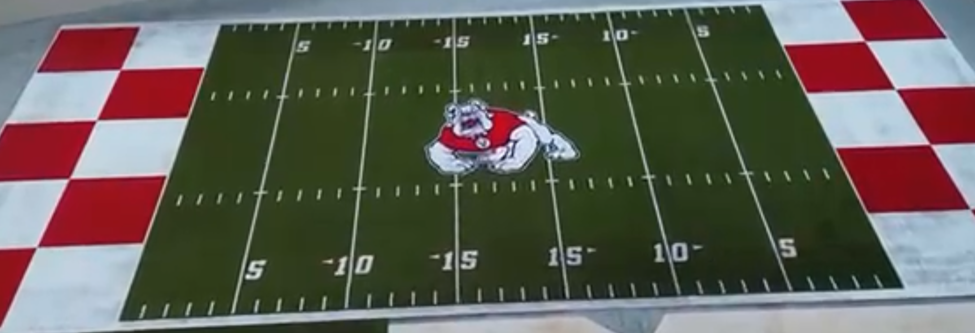 A rectangular sports rug with a football field design and a cartoon bulldog mascot in the center, surrounded by a red and white checkered border.