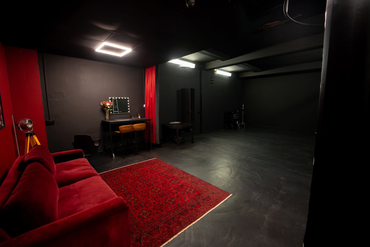Blackout Studio at STU 22 Wapping: 26ft by 19ft matte black shooting floor with red velvet sofa, vintage rug and lit mirror station