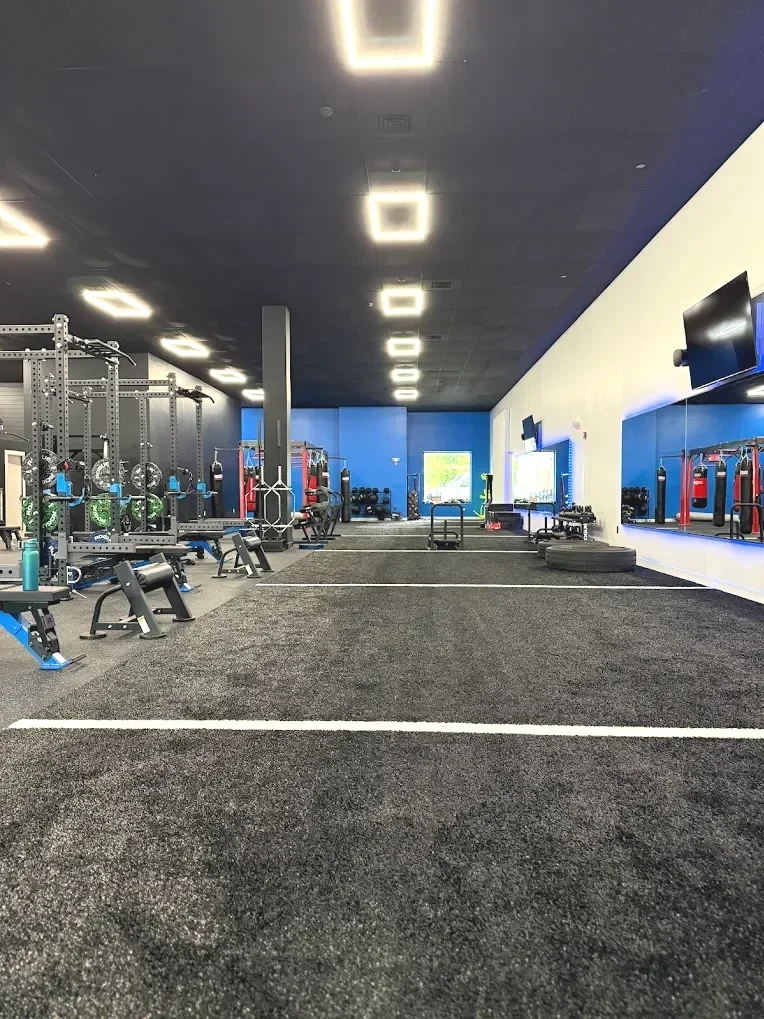 Empty gym with workout benches, weights, and fitness equipment, illuminated by ceiling lights.