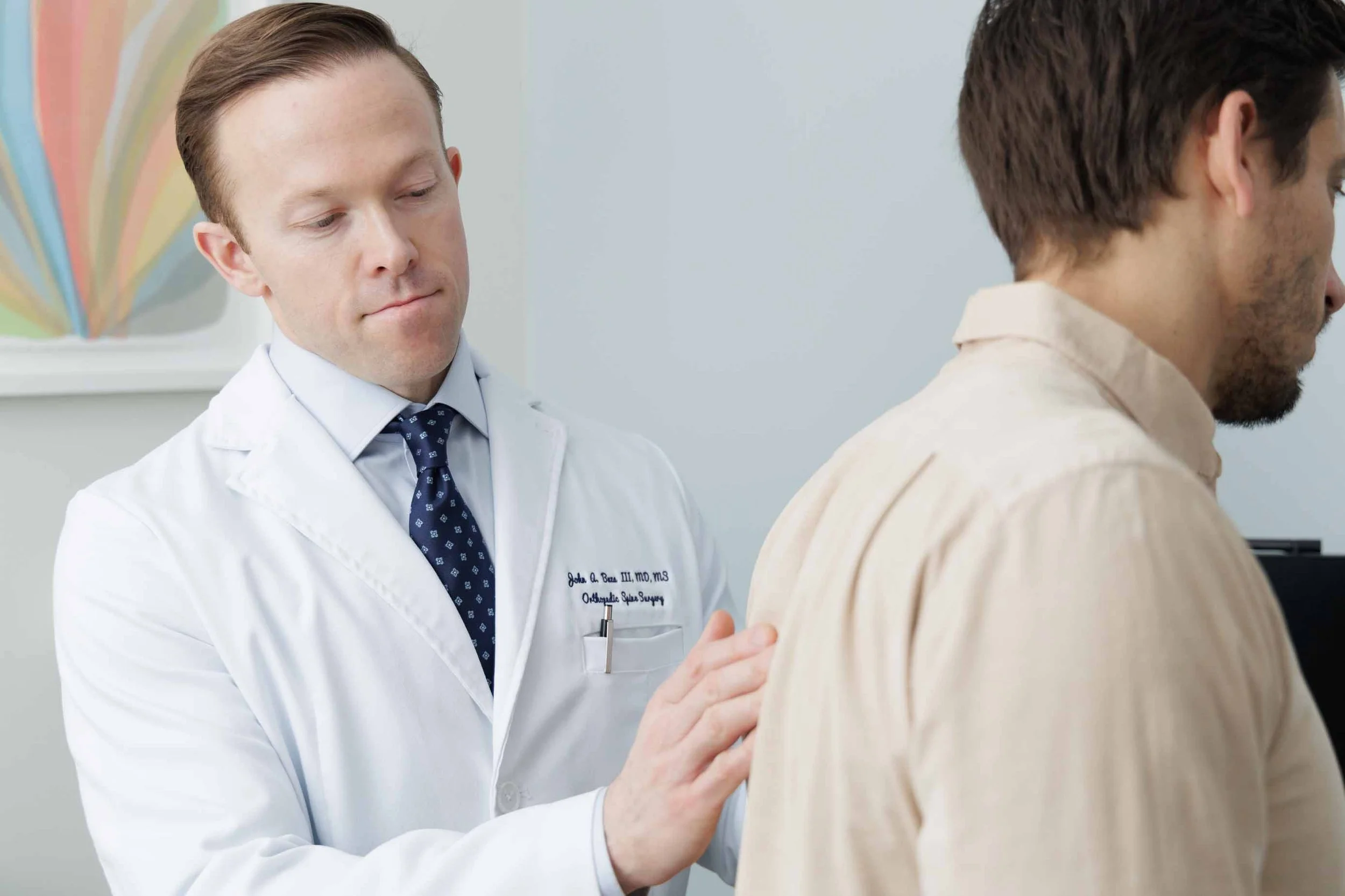 Doctor performs a physical examination on a patient by checking his back in a medical office.