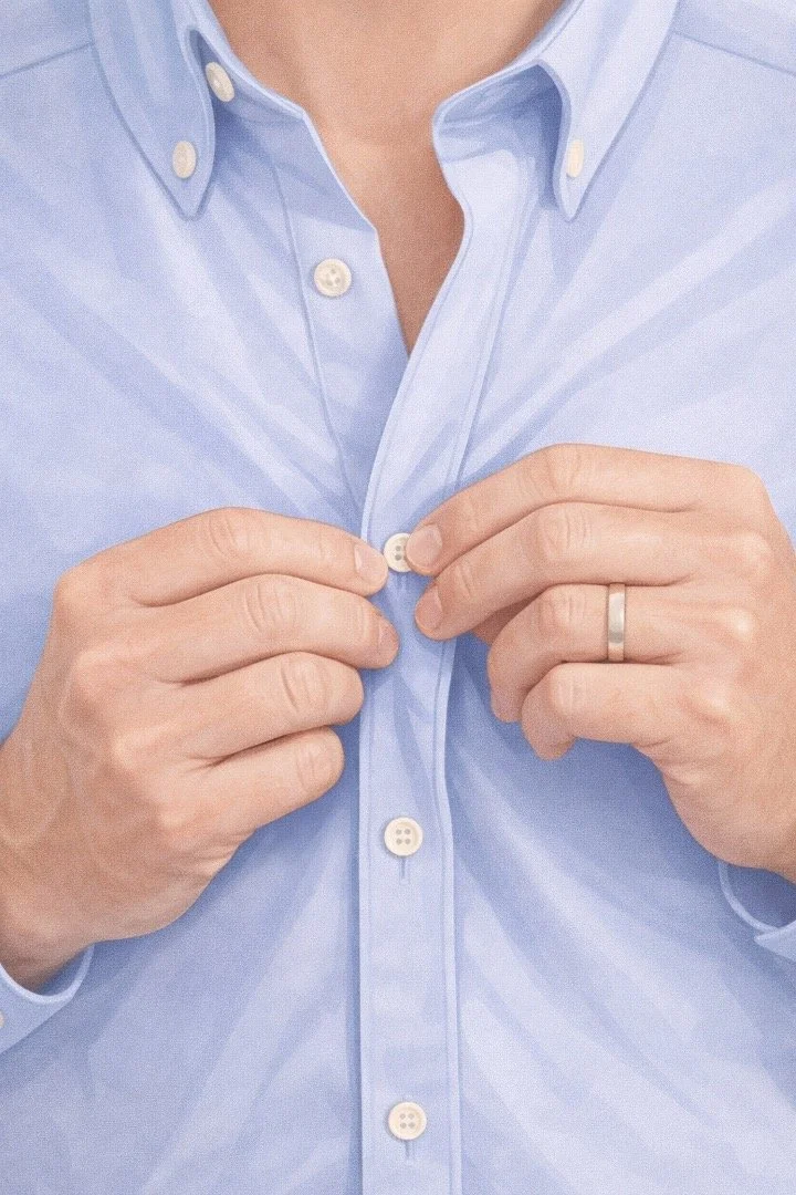 A person buttoning up a light blue dress shirt, showing only the torso and hands.