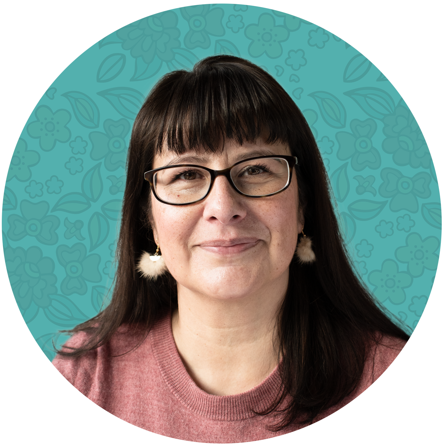 Felicia Dewar. Founder, miskamâsowin. Portrait of a woman with dark hair, glasses, and earrings, smiling, wearing a pink sweater, with a teal background decorated with floral patterns.