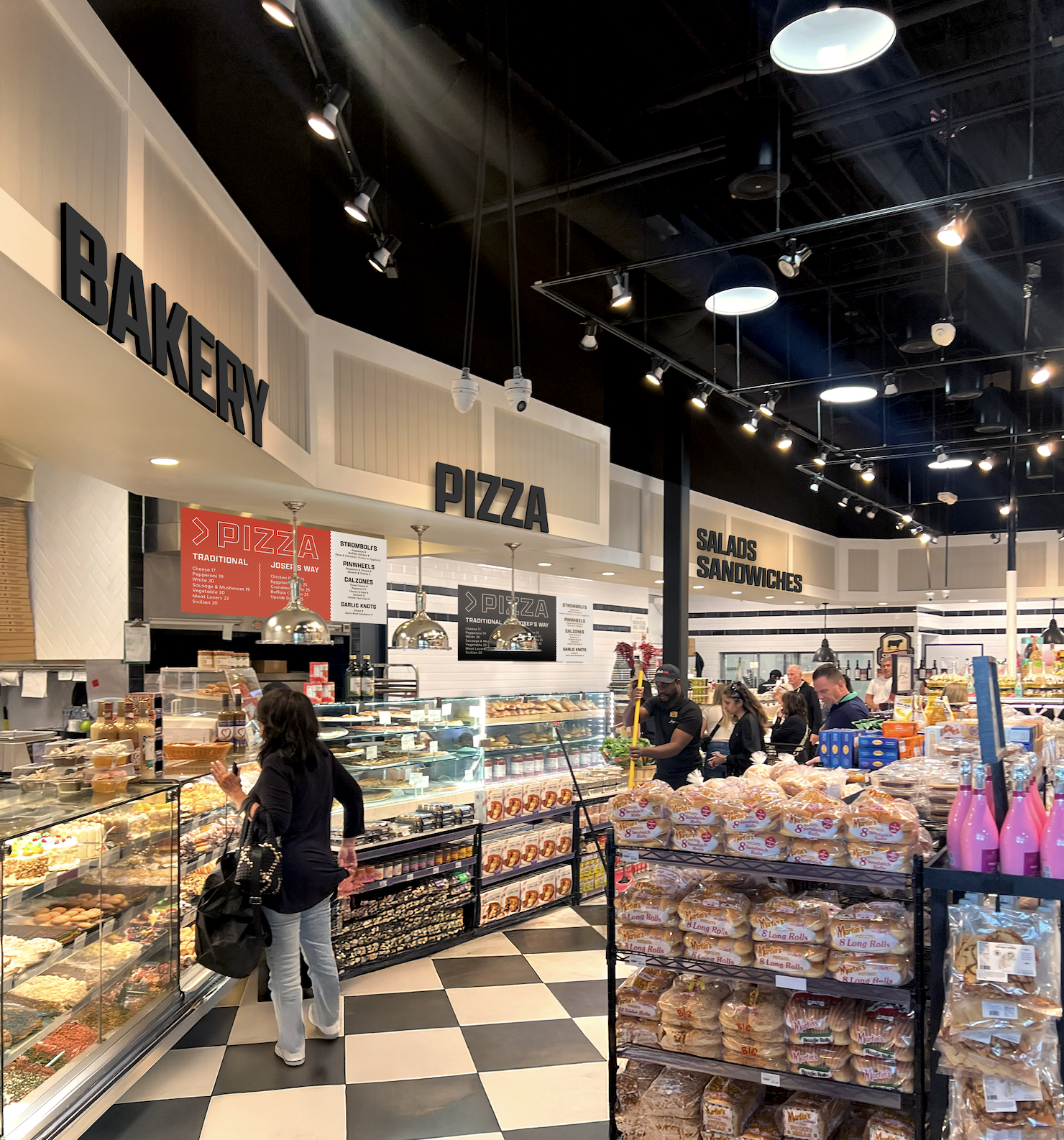 Inside a bakery and pizza shop with grocery shelves. Customers browse baked goods and bread.
