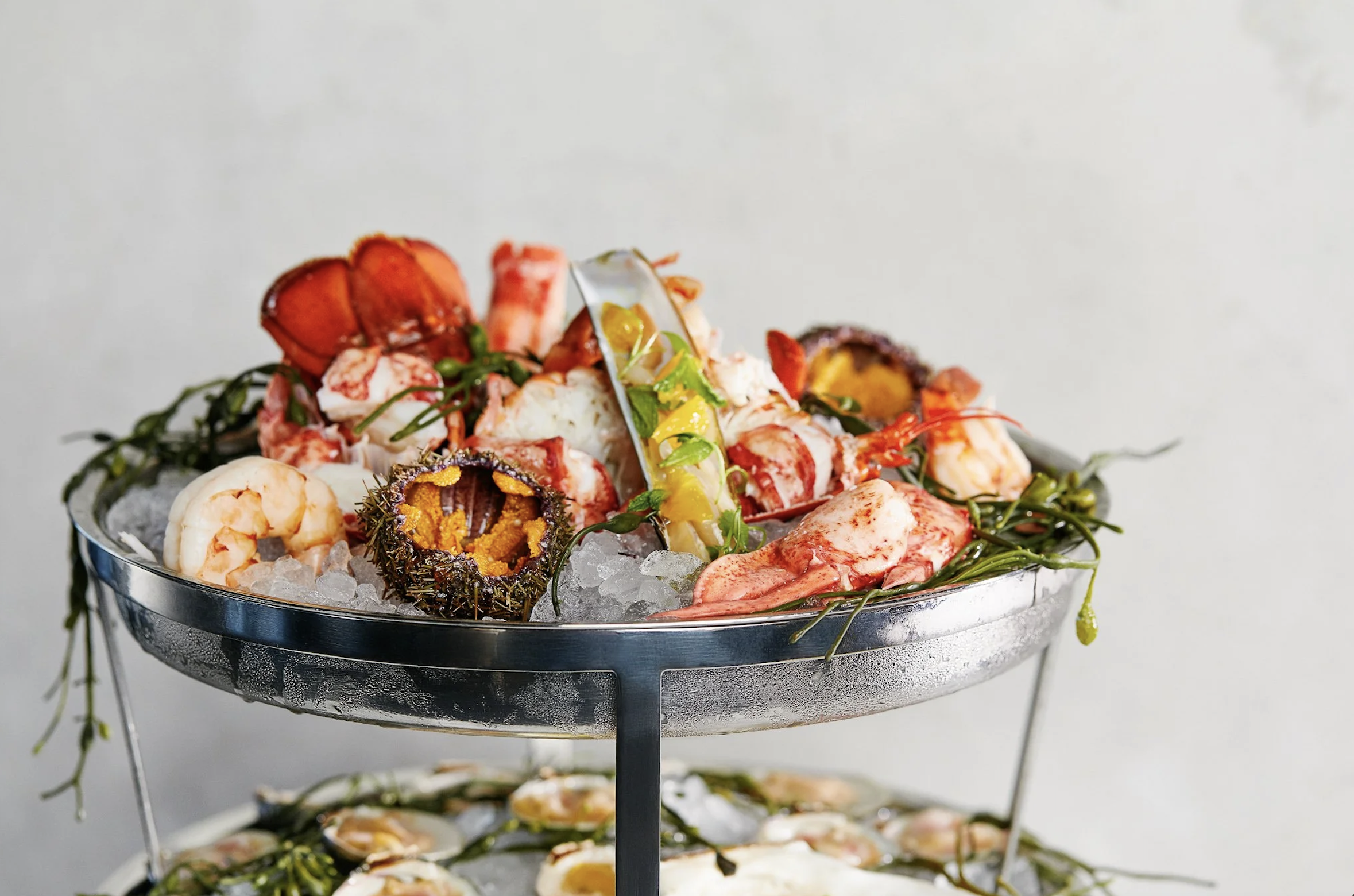 Seafood platter with lobster, shrimp, oysters, and crab, served on ice in a metal dish over a two-tiered stand. Robert Ranfranz branding, design and ecommerce.