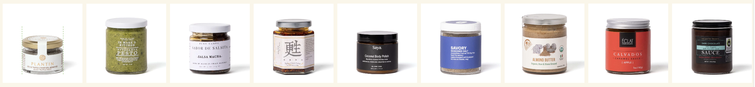 A row of nine small jars containing various food items and condiments, including pesto, salsa, chili sauce, coconut body polish, seasoned salt, almond butter, caramel sauce, and dark chocolate sauce.