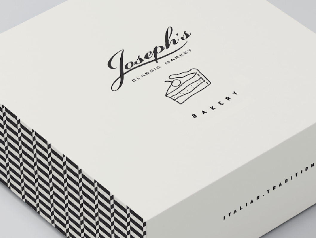 A white box with the logo and name of Joseph's Classic Market Bakery, featuring a line drawing of a slice of cake and a fork. The side of the box has a black and white chevron pattern.