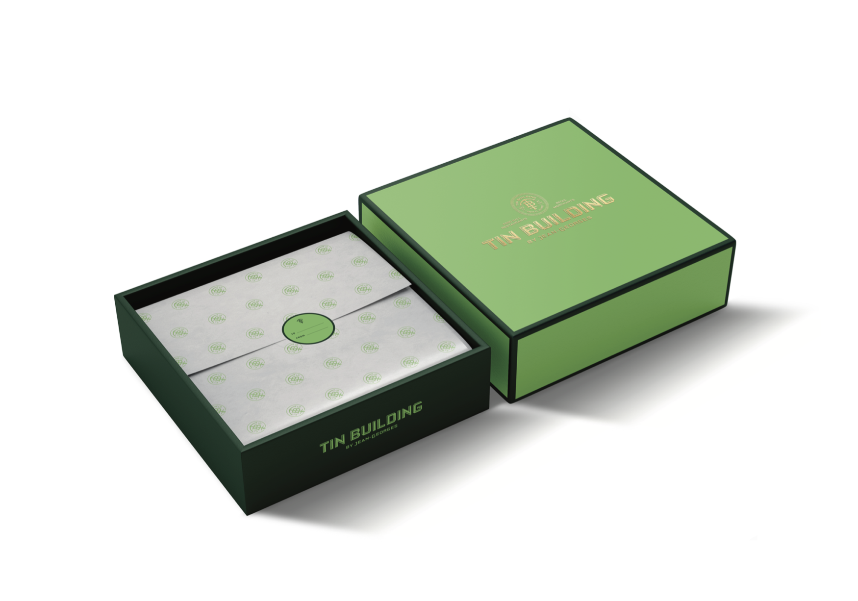Open green and black box labeled 'Tin Building by Jean-Georges', containing decorative paper with green logo pattern and a round green sticker inside.