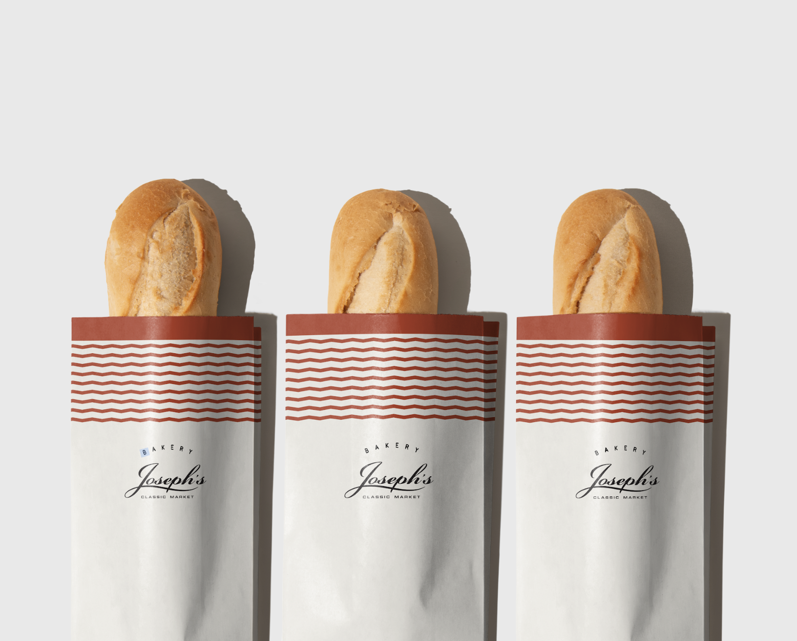 Three sandwiches with hot dog buns in white paper wrappers labeled 'Joseph's Bakery' in front of a plain gray background.