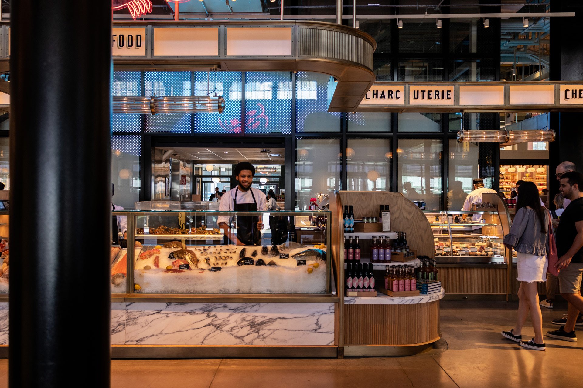 Inside a modern food market or restaurant, a display case filled with various seafood items like fish and shells is in the foreground. Robert Ranfranz branding, design and retail.