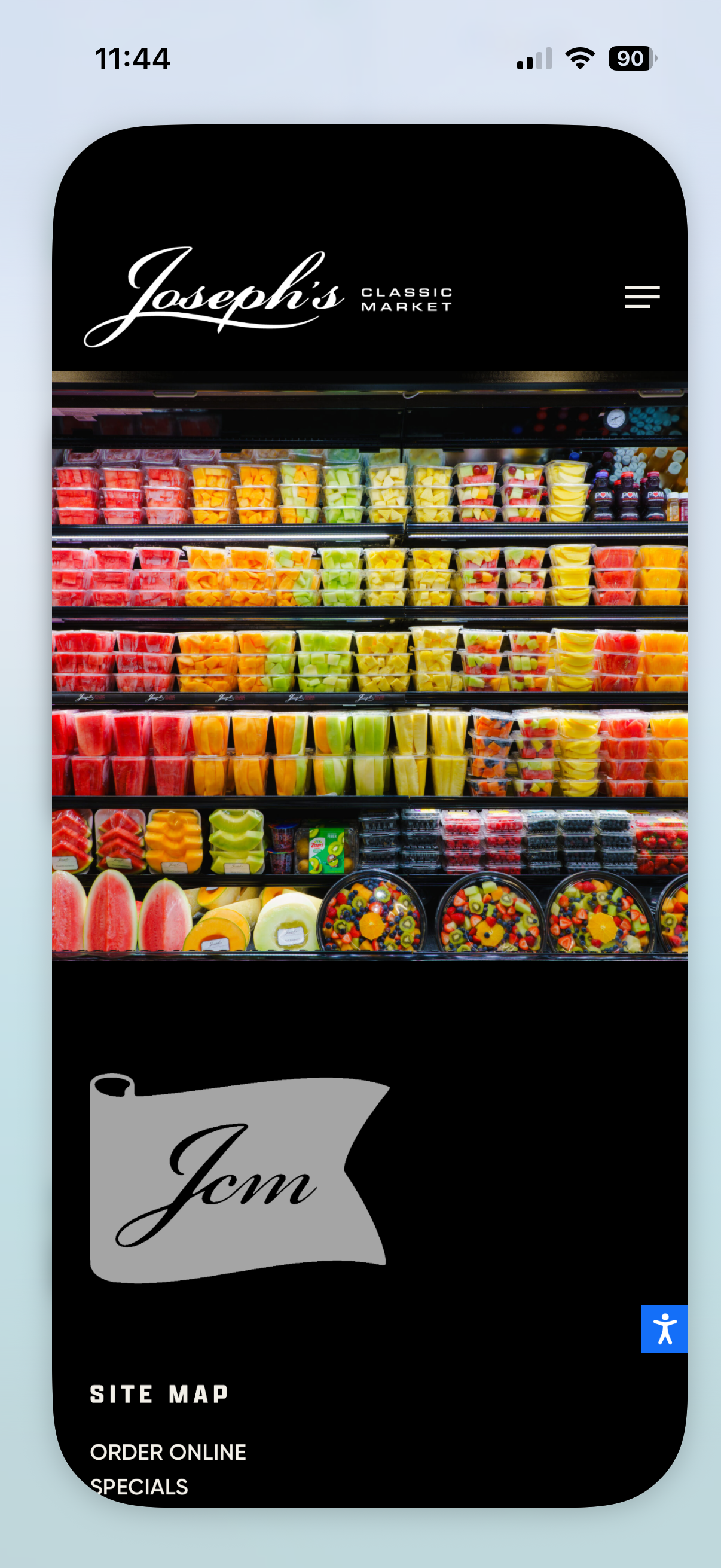 Screenshot of a smartphone displaying the website of Joseph's Classic Market, showing a colorful display of pre-cut fruits and fruit bowls in a grocery store. The top part features the store's logo, and the lower part shows menu options.