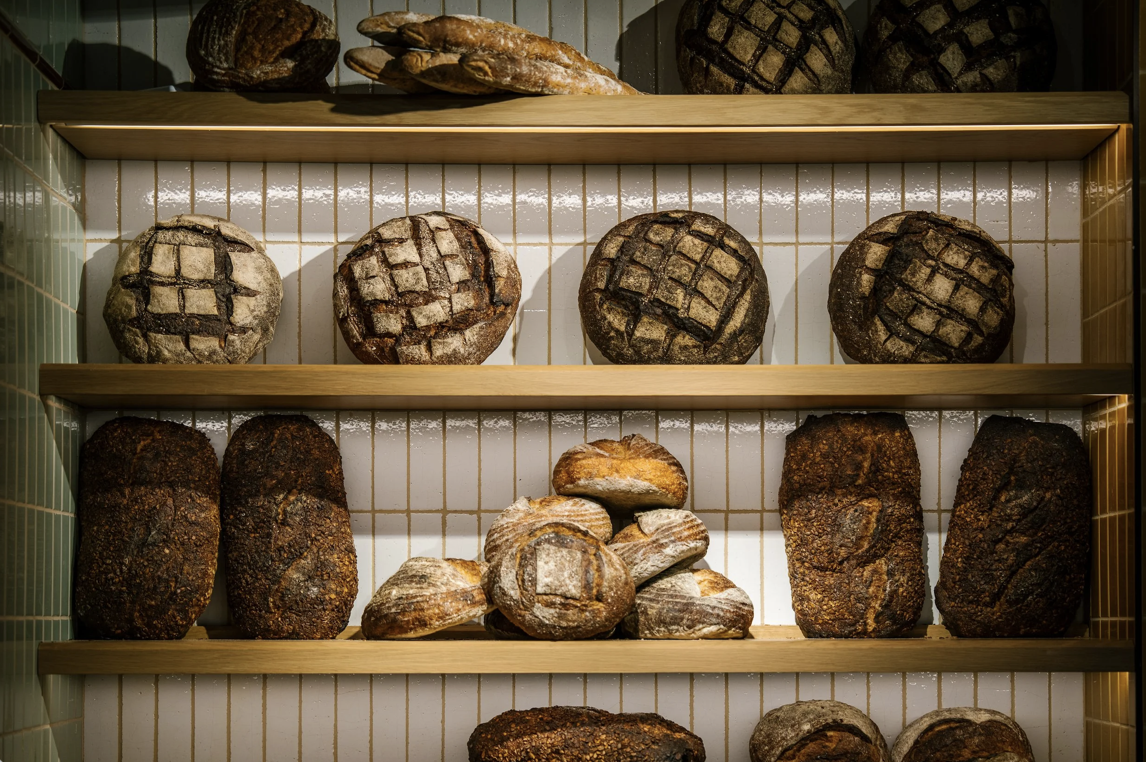 A display of various loaves of bread arranged on wooden shelves, with some loaves having a grid pattern scored on top. Robert Ranfranz branding, design and packaging.
