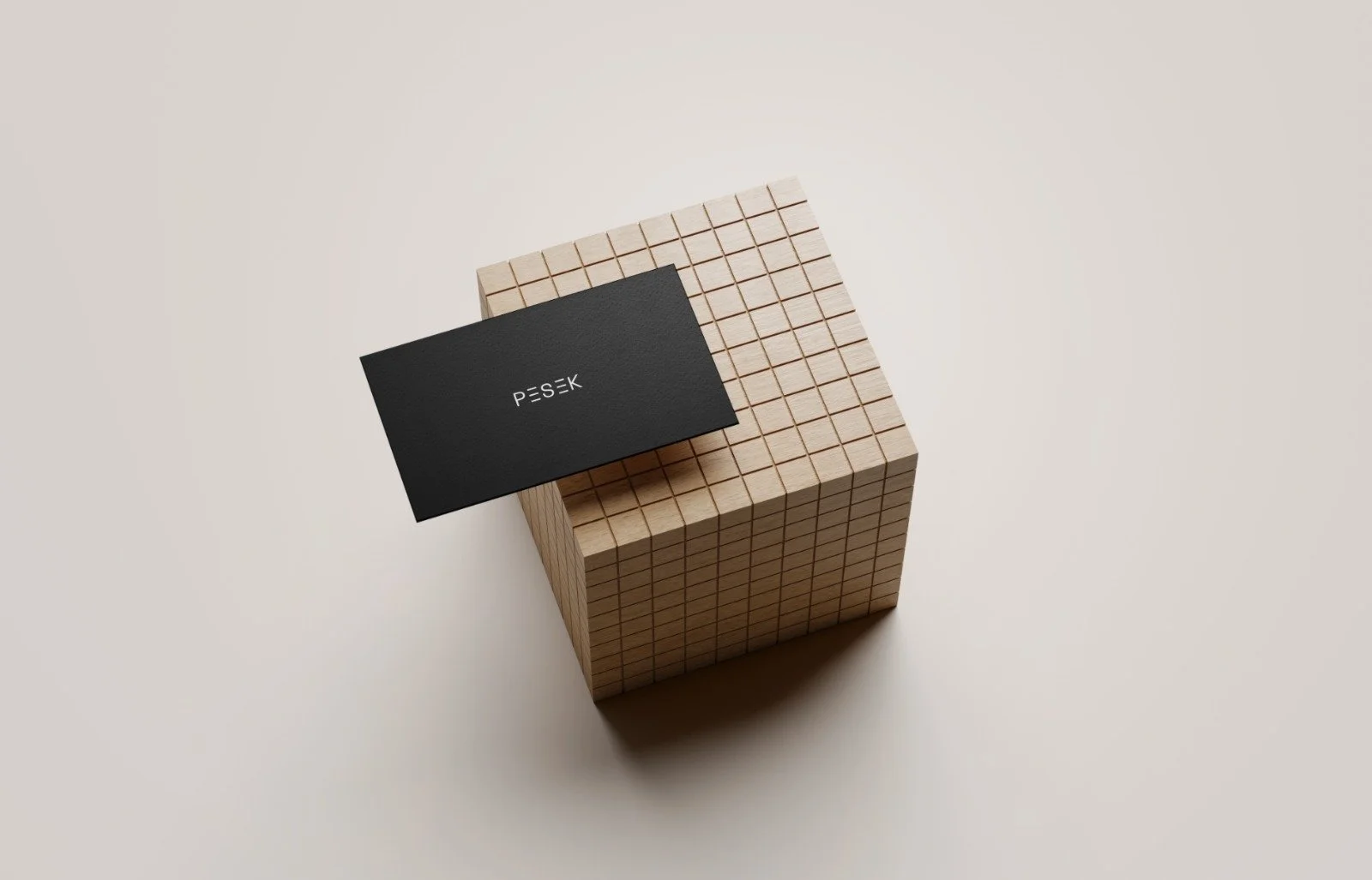 A black business card with the word 'PESEK' placed on a wooden grid cube, set against a plain light background.