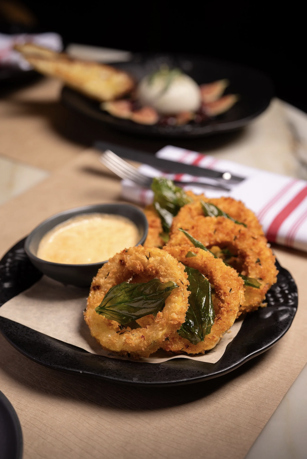 Close-up of fried calamari rings garnished with herbs and served with a dipping sauce on a black plate. Robert Ranfranz branding, design and ecommerce.