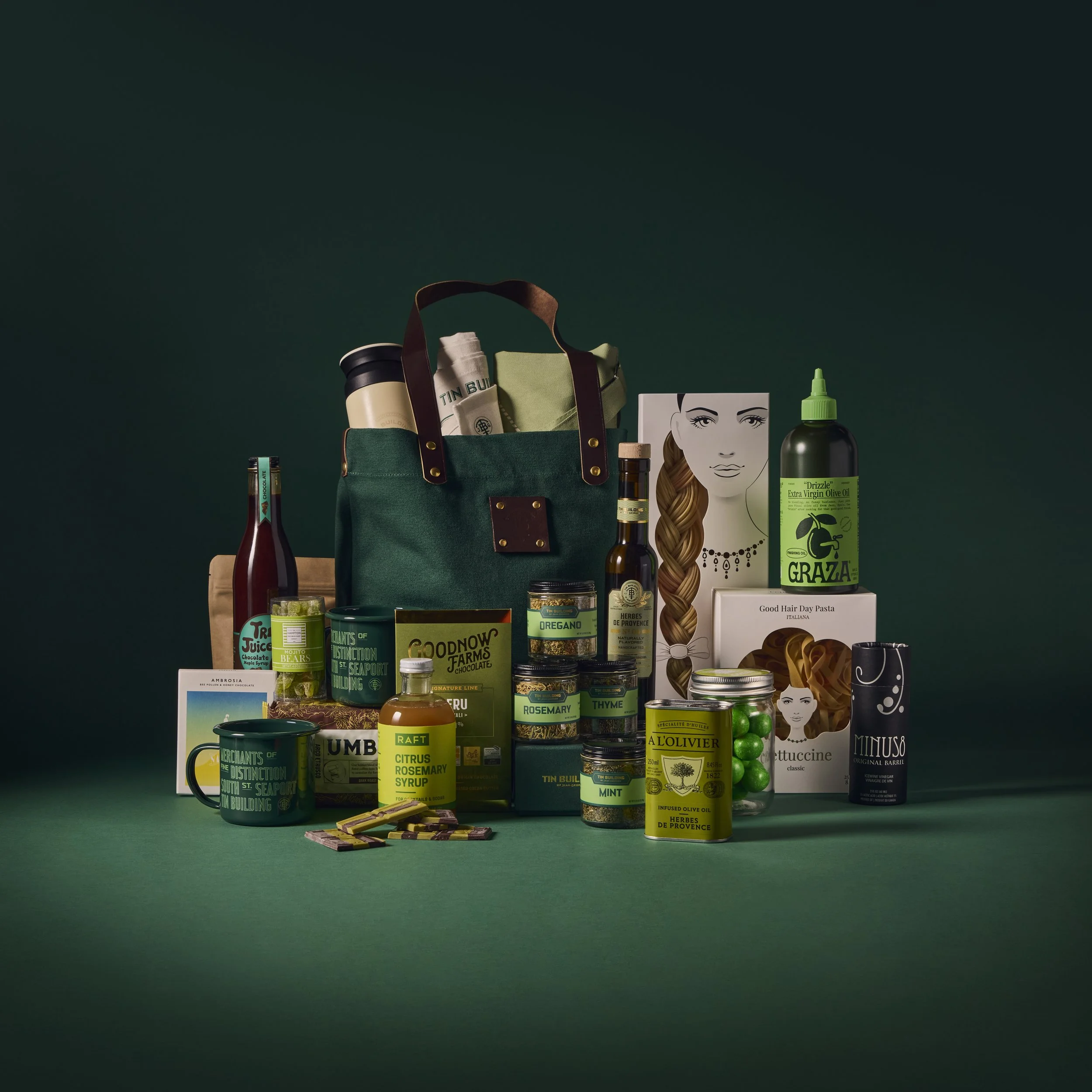 A collection of assorted food, beverages, cosmetics, and personal care products arranged in front of a green bag with a dark green background.