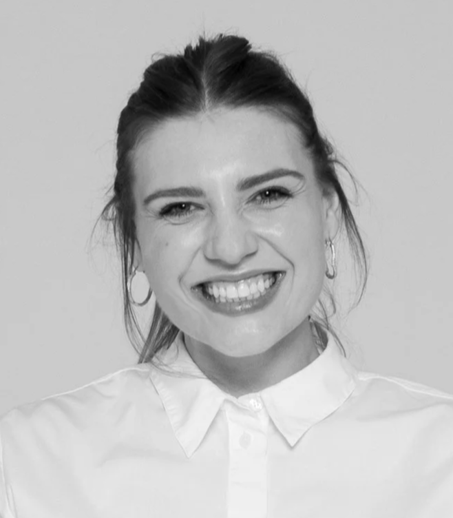 Black and white photo of a smiling woman with her hair pulled back, wearing hoop earrings and a collared shirt.