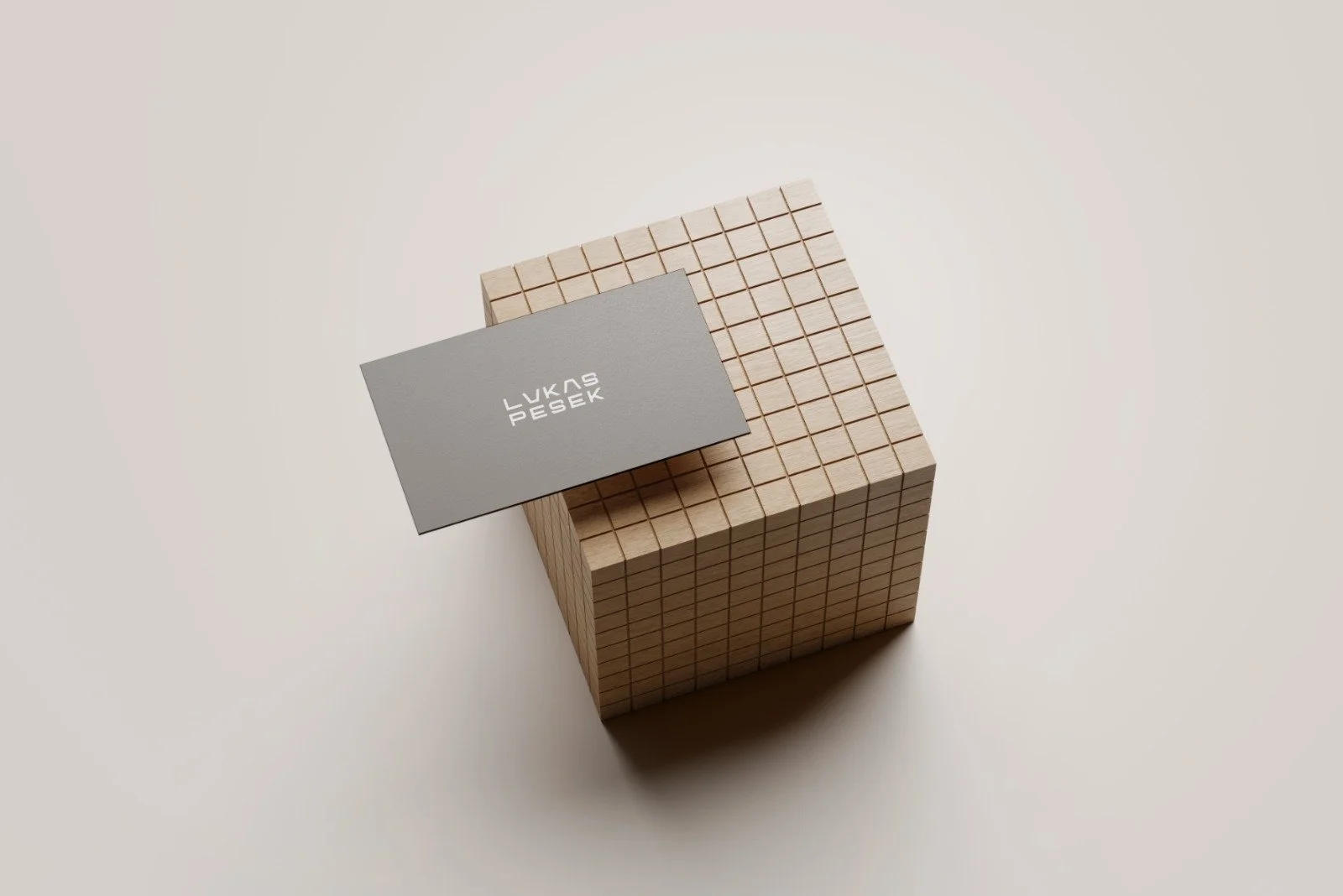 A gray business card with white text resting on a 3D wooden cube composed of small square blocks, on a plain light background.