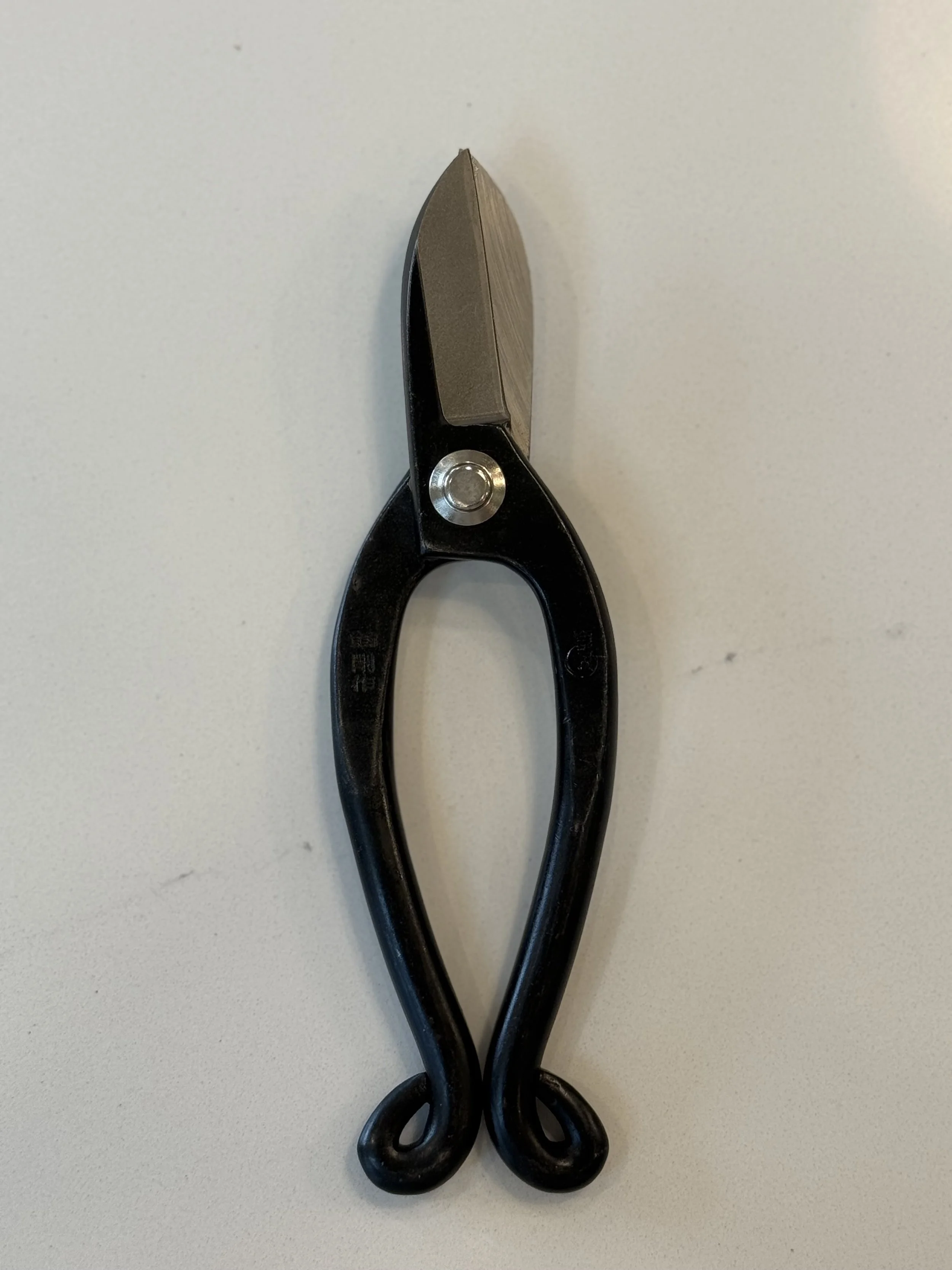 Close-up of a pair of black scissors with black handles resting on a white surface.